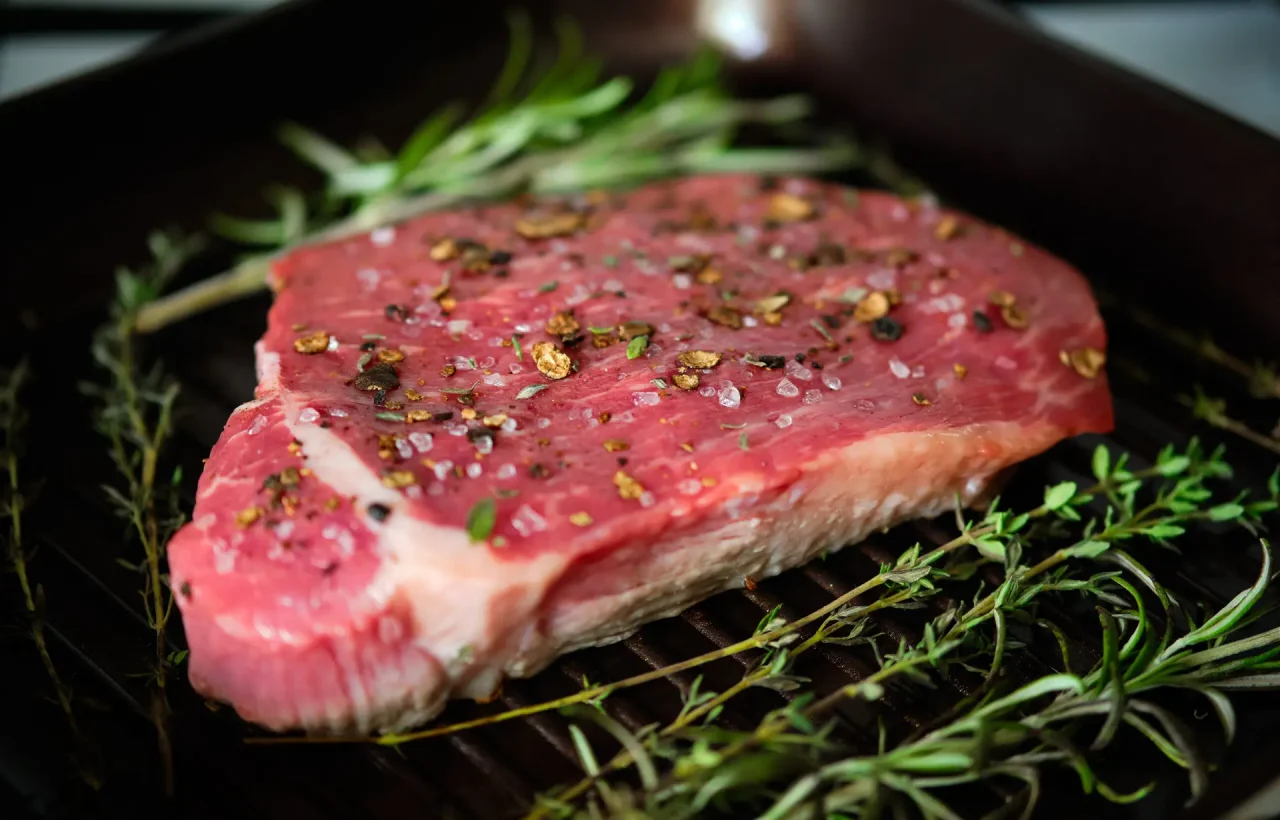 Raw steak with spices on grilling pan with rosemary